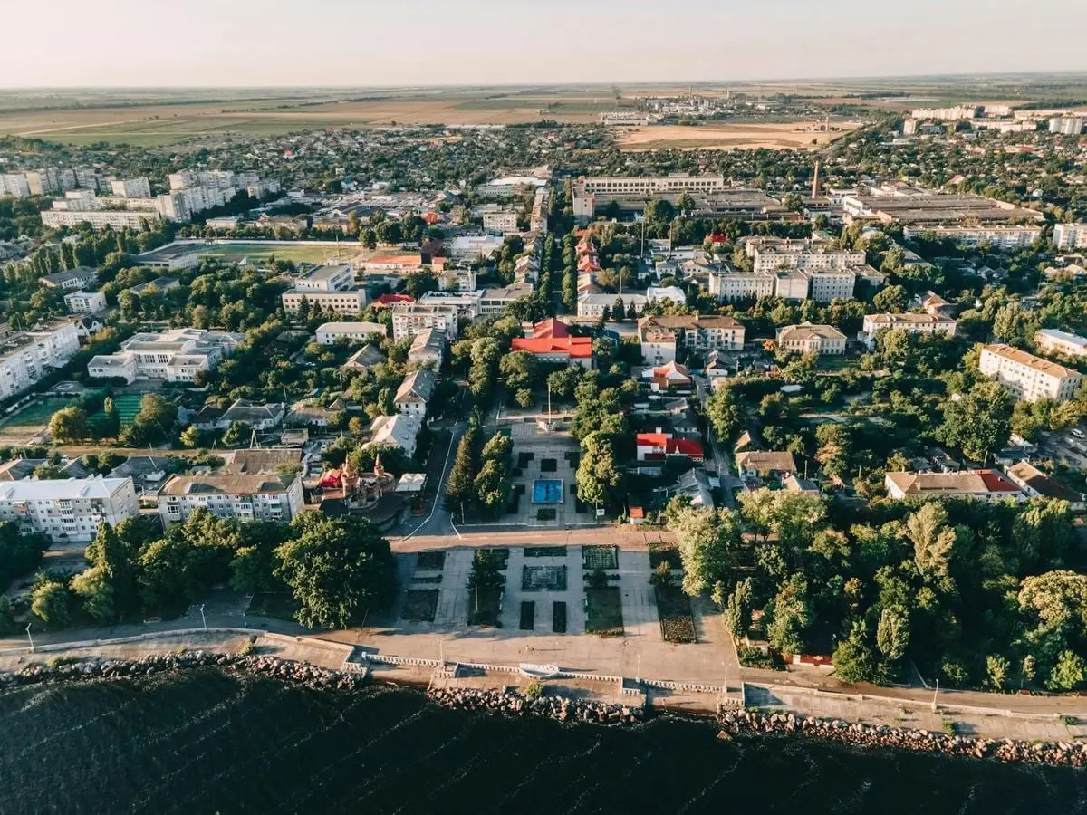 Aerial view of a peaceful coastal town showcasing greenery, buildings, and a waterfront area during summer.