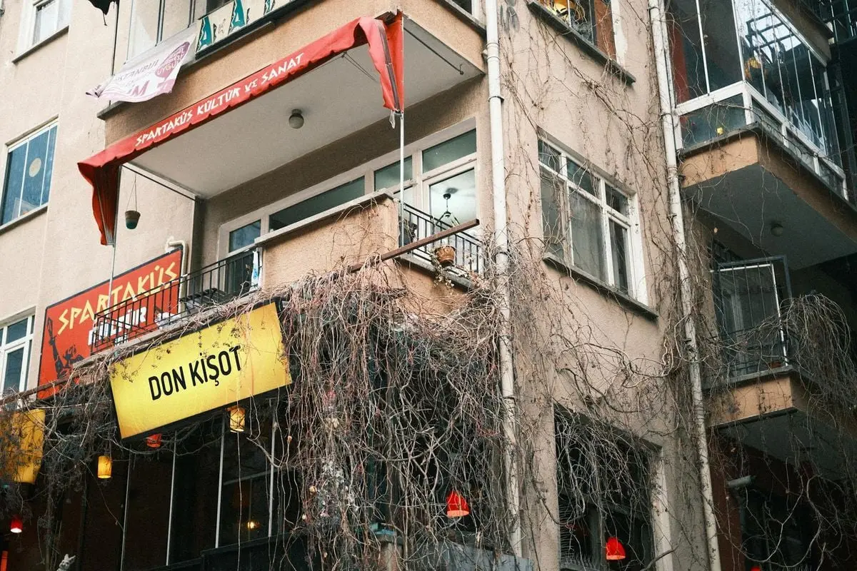 Low angle shot of an urban building with ivy-clad balconies and vibrant signs in a Turkish town.
