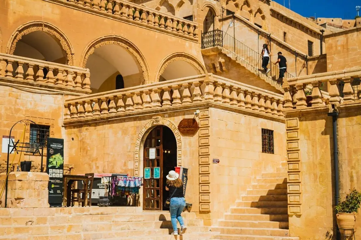 Sunlit stone building with visitors at Midyat, Turkey, showcasing local architecture.