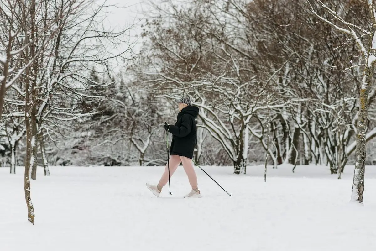 A person in winter clothing walking through a snow-covered park with leafless trees.