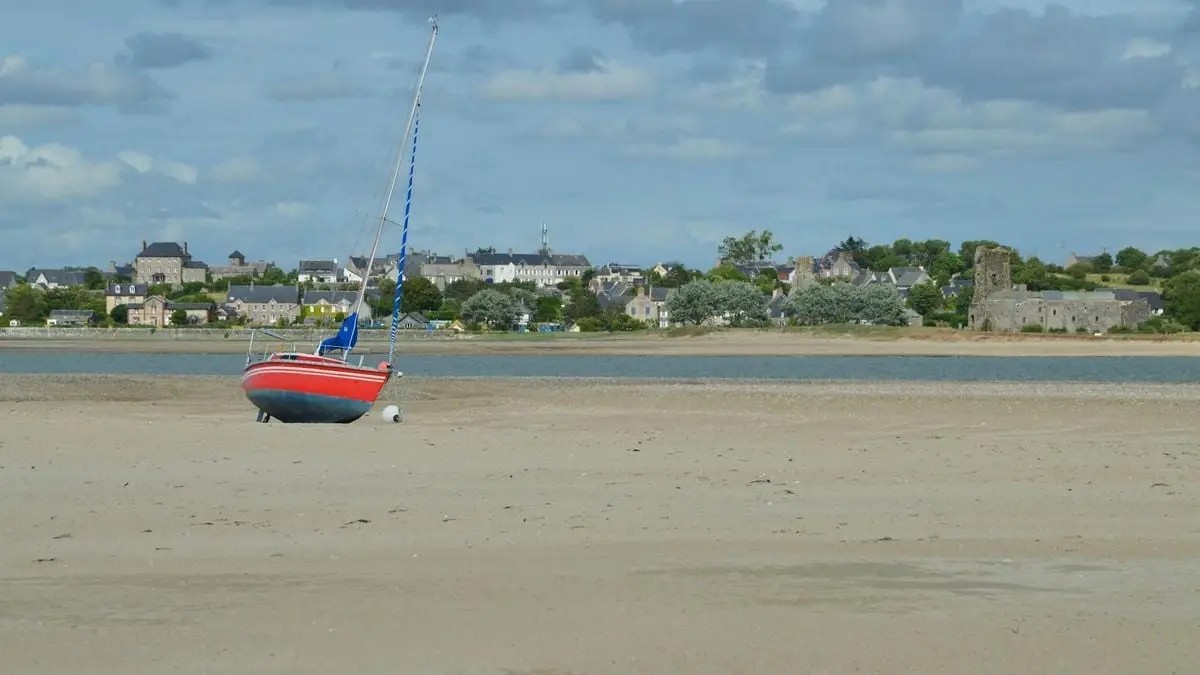A red sailboat rests on the sandy shores of Agon-Coutainville in Normandy, France.