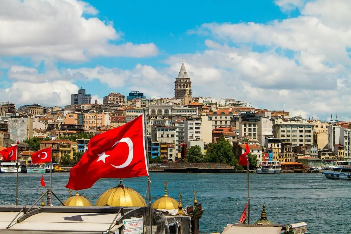 Cityscape view of Istanbul with Galata Tower and Turkish flags by the waterfront, showcasing vibrant urban life.