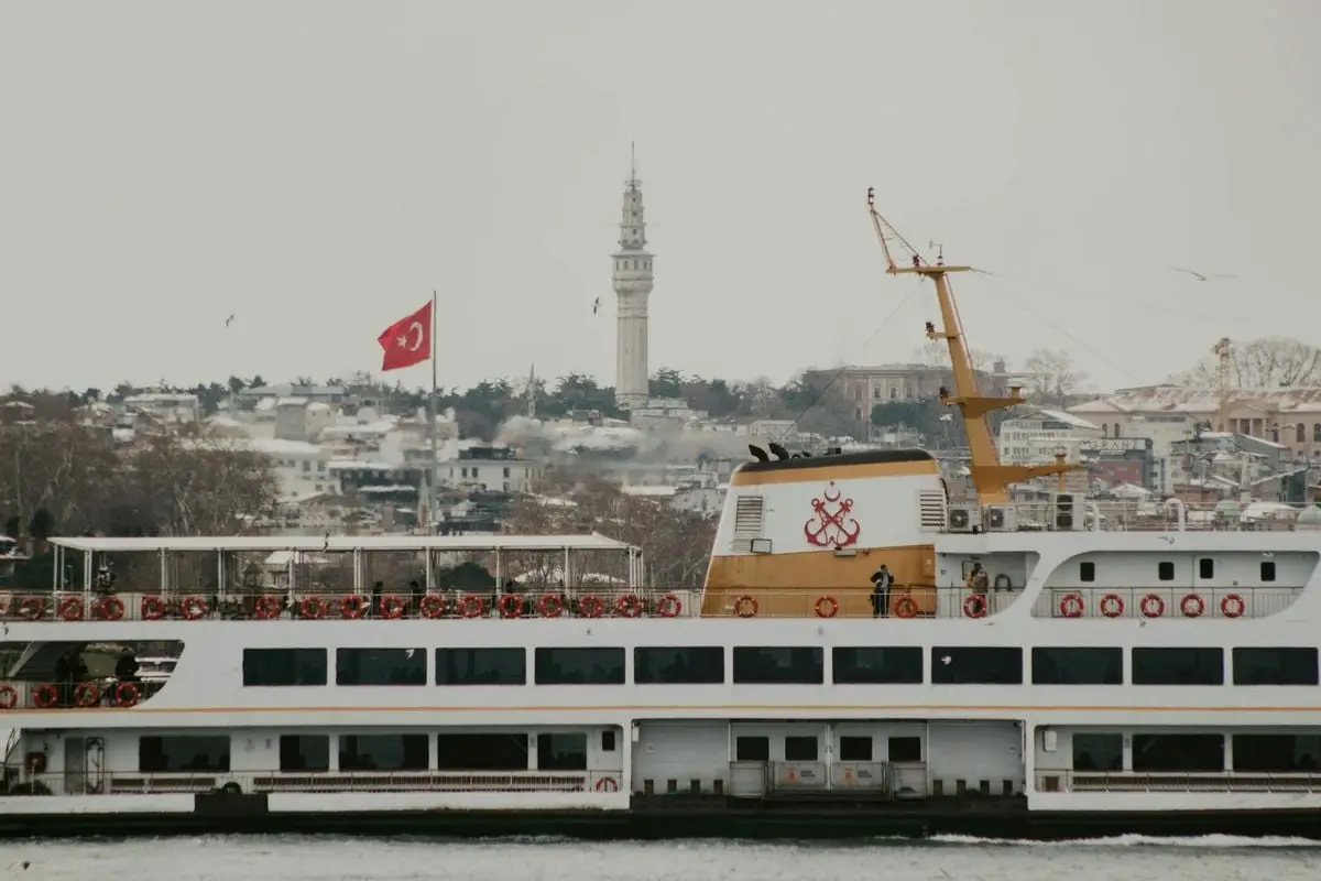 Ferry sailing in Istanbul with historic tower and Turkish flag in winter scenery.