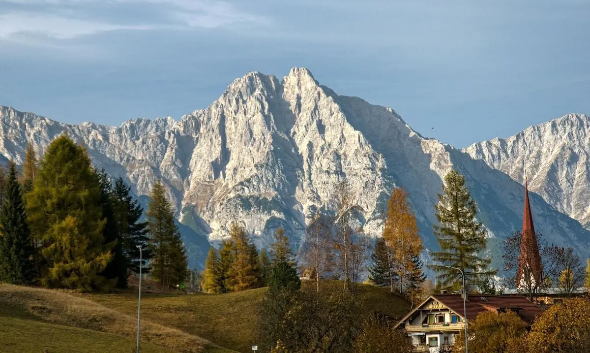 Idyllic alpine village nestled at the base of majestic mountains during fall, showcasing rustic charm and natural beauty.