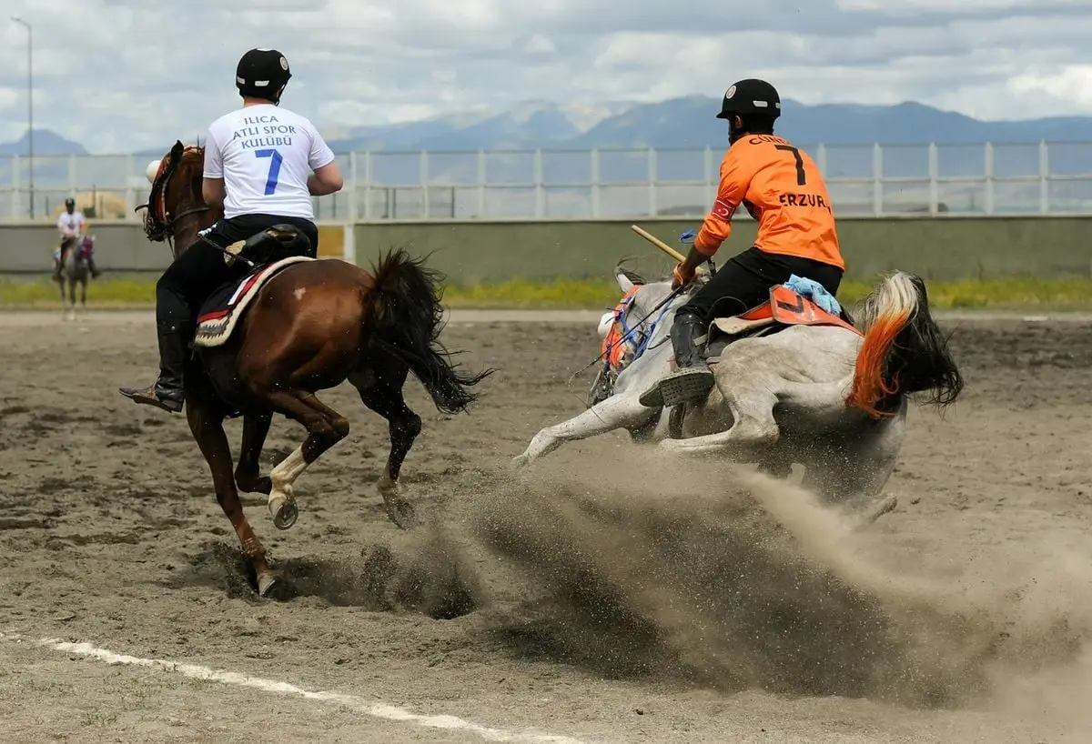 Two horseriders compete intensely in a traditional Turkish equestrian race, kicking up dust.