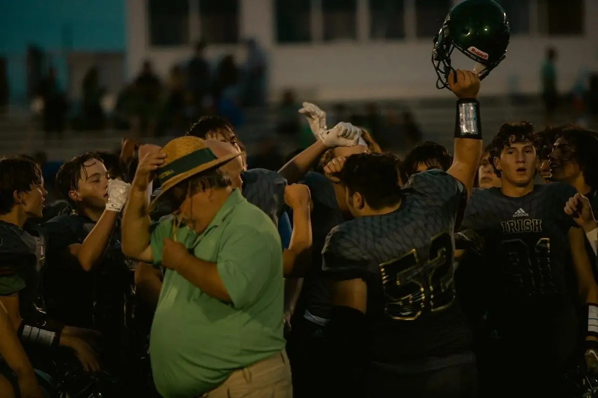 High school football team celebrates victory on the field at night.