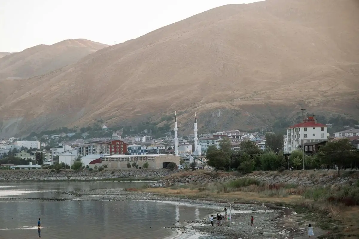 Serene view of a lakeside town with a mosque and mountains in Turkey at dusk, perfect for travel inspiration.