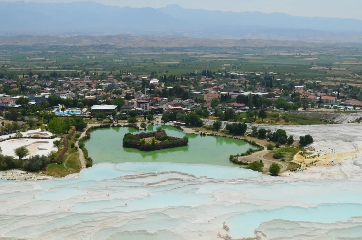 Scenic view of Pamukkale's travertine terraces and nearby village under a clear sky.