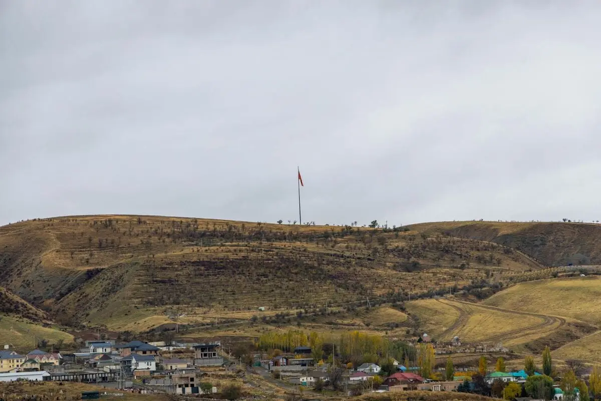 A scenic view of a hillside village with a prominent flagpole on a cloudy day.