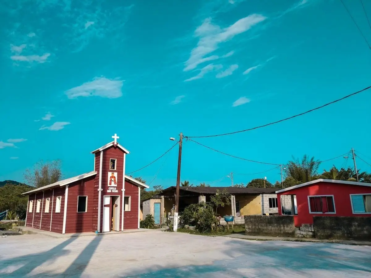 A picturesque village church surrounded by houses in Guarujá, Brazil, under a clear blue sky.