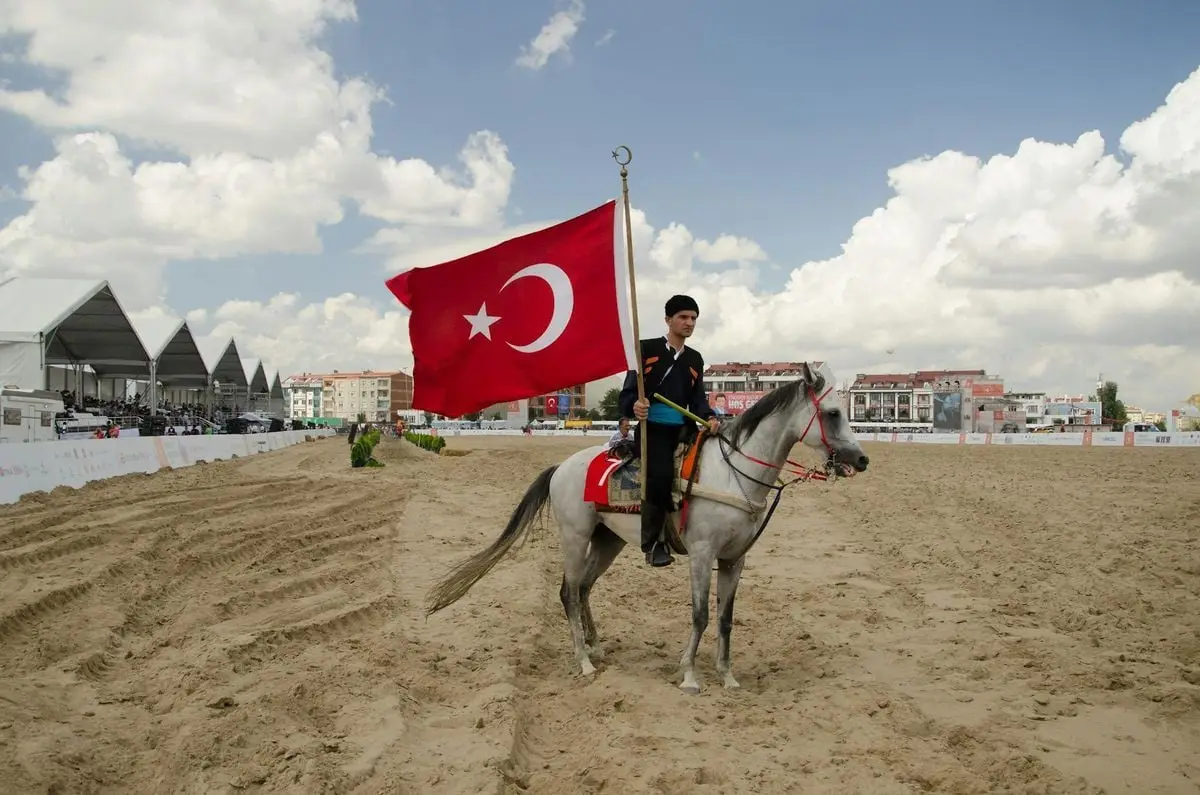 A man on horseback holding the Turkish flag at an equestrian event in İstanbul.