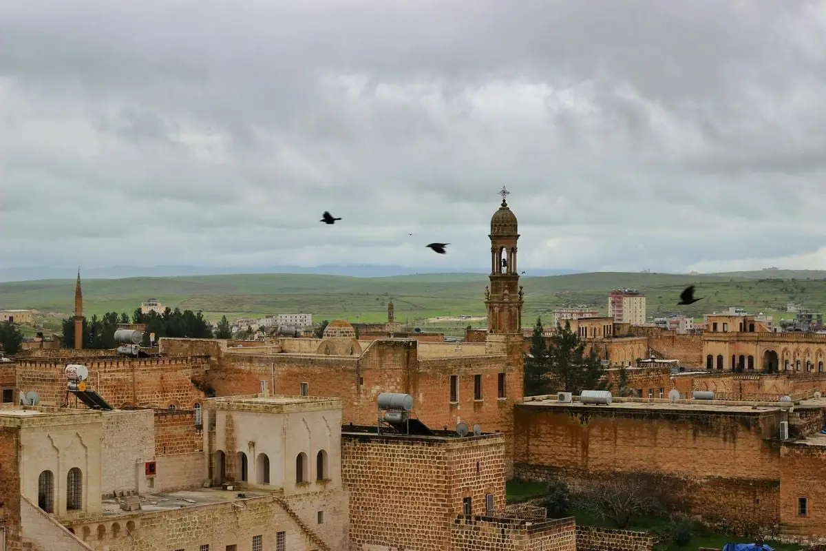 Scenic view of Midyat with ancient buildings and historic towers under cloudy skies.
