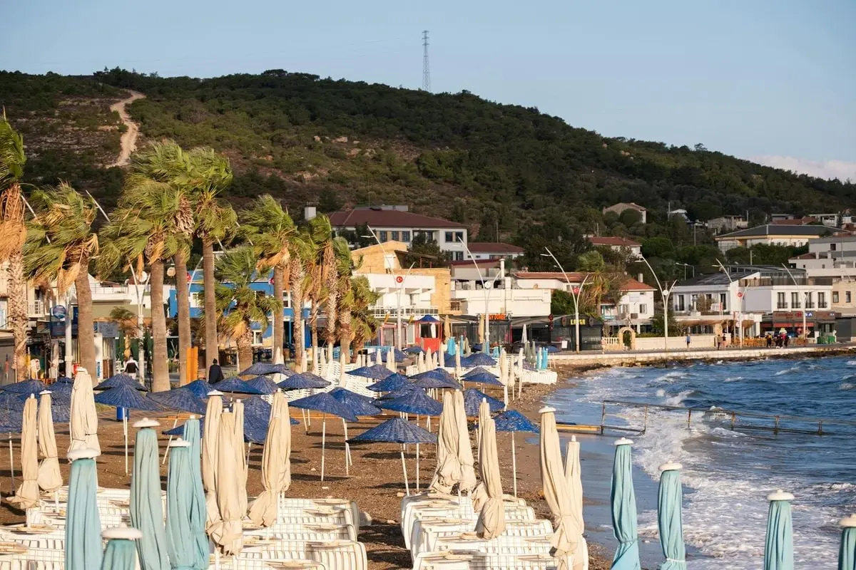 Peaceful beachfront scene in Foça, İzmir, Türkiye, showcasing empty sunbeds and umbrellas at sunset.