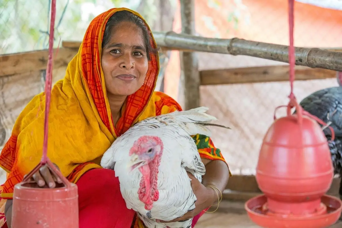 A woman with a turkey in a farm setting in Chattogram, Bangladesh.