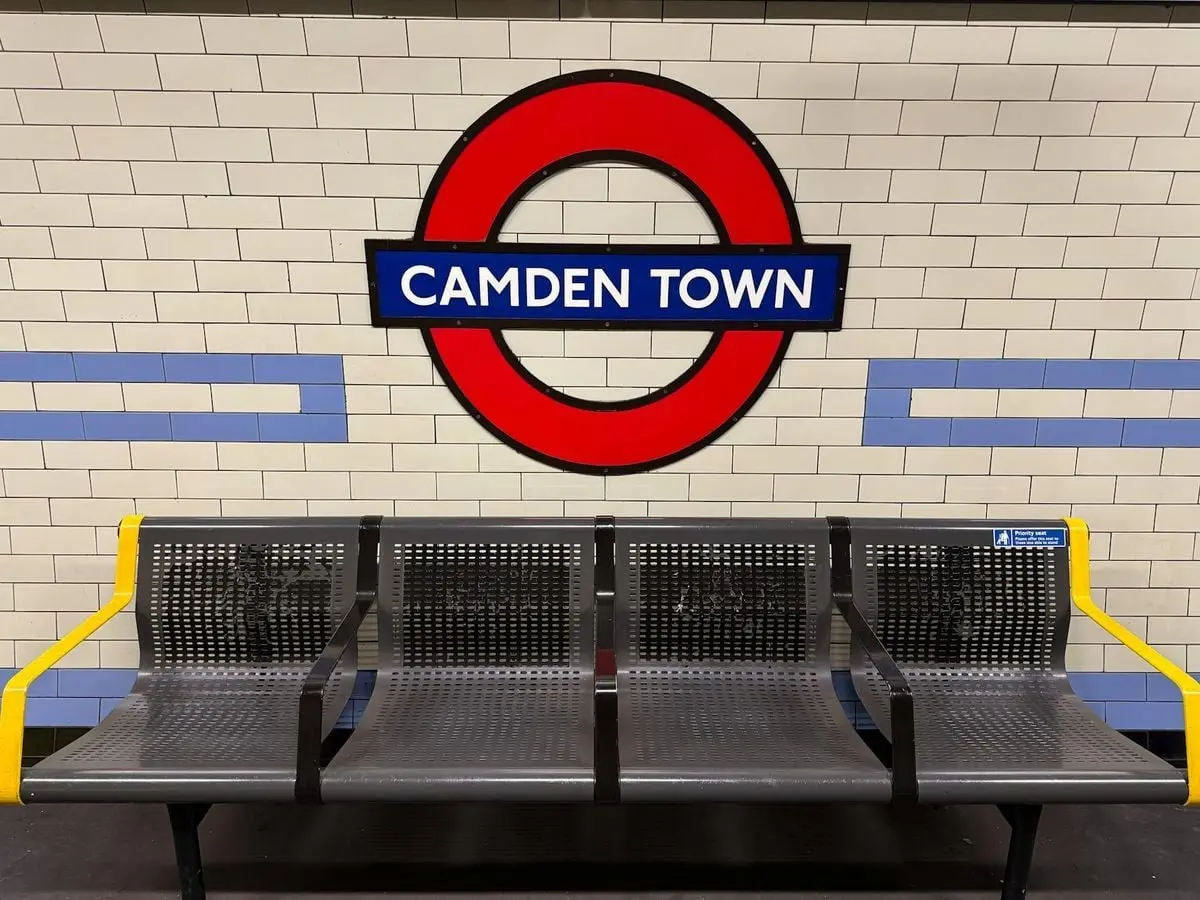 A view of Camden Town station sign with an empty bench in a London Underground setting.
