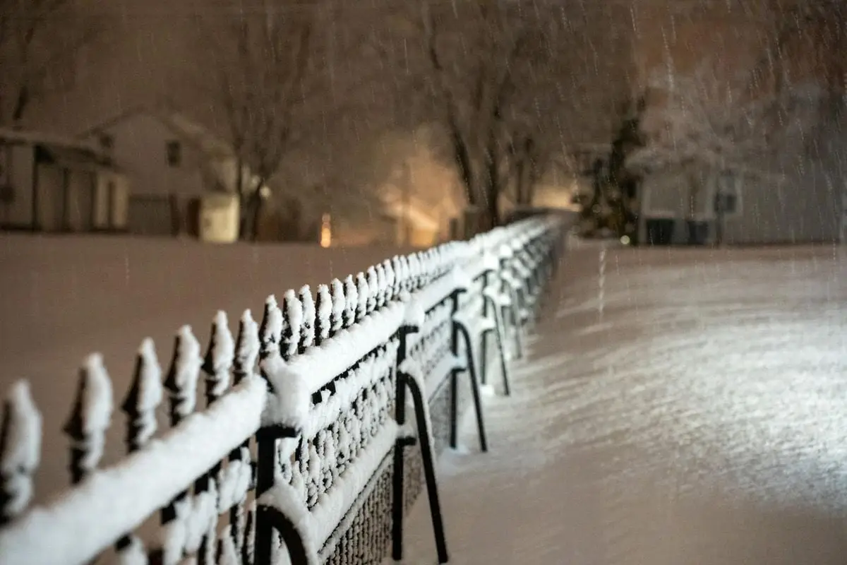 Snow-covered metal fence during night snowfall in Wabasha, MN village.