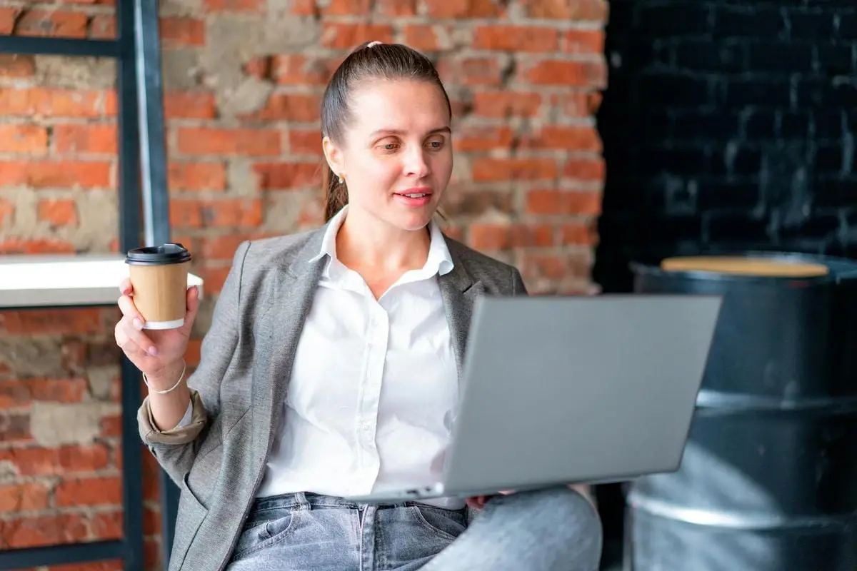 Woman enjoying a coffee while working remotely on a laptop indoors.