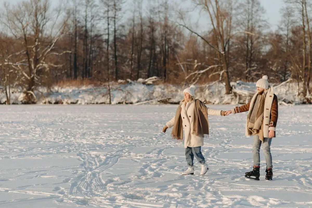 Couple enjoying a winter day ice skating on a snow-covered frozen lake.