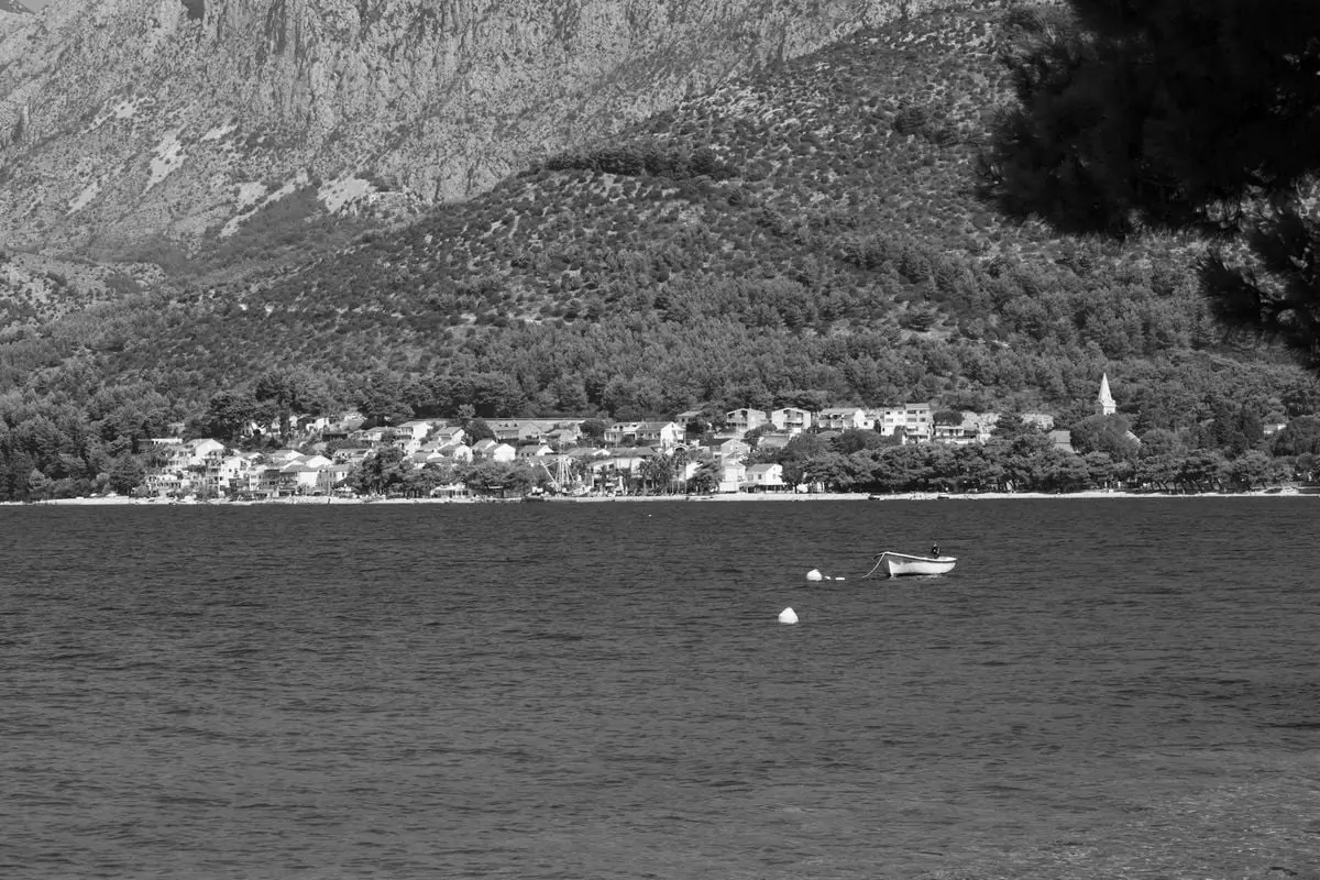 Black and white photo of Zaostrog's charming village by a serene coast with rugged mountains.