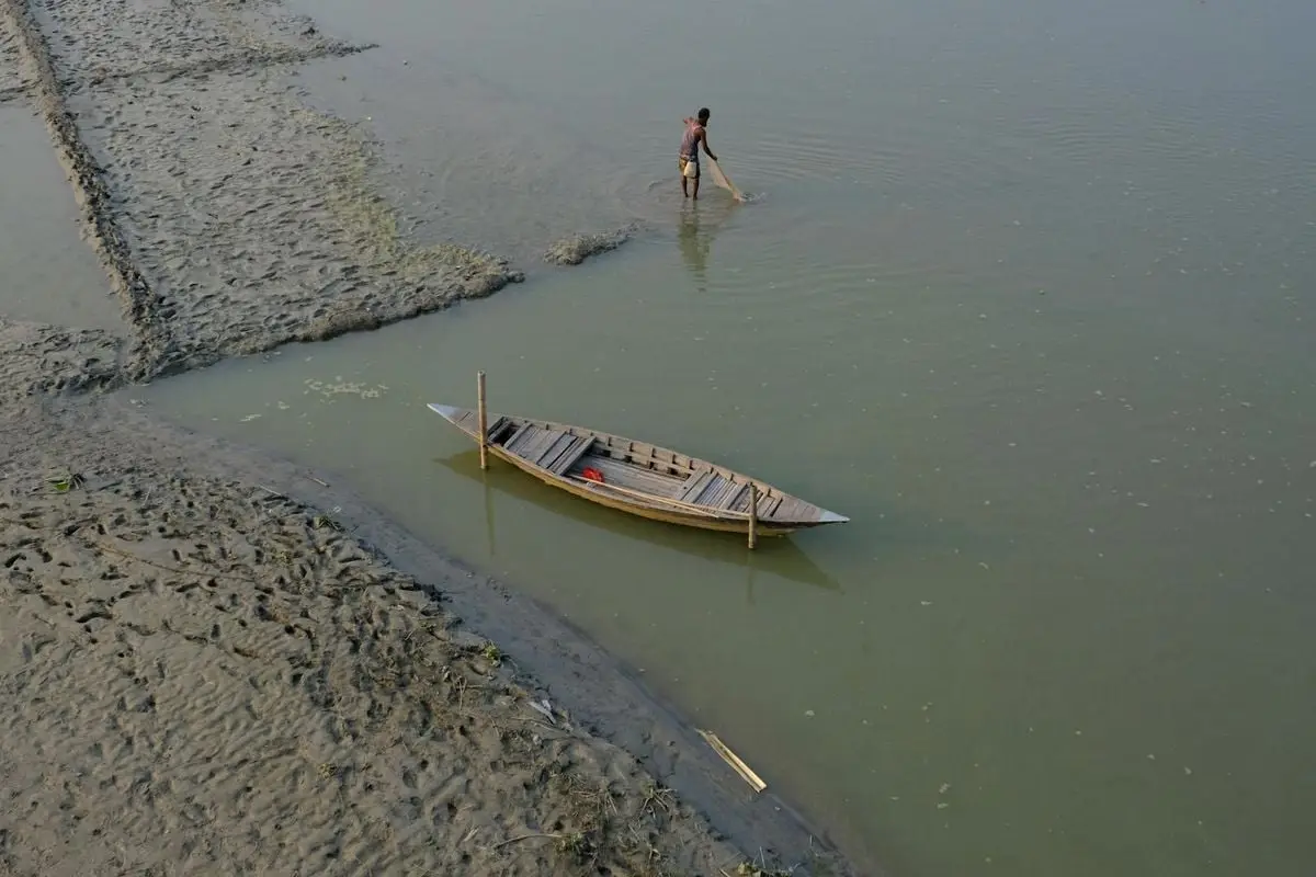An aerial shot of a fisherman with a wooden boat in calm river water, carrying a fishing net.