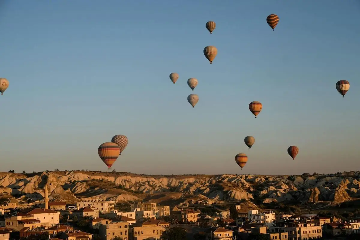 Breathtaking view of colorful air balloons flying in blue cloudless sky above stone mountains near buildings in city in sunny evening