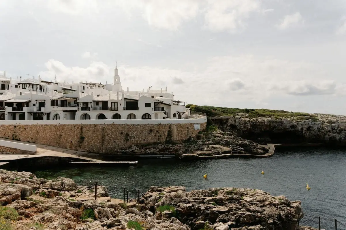 Charming white buildings by rocky coast in Ciutadella de Menorca, Balearic Islands, Spain.