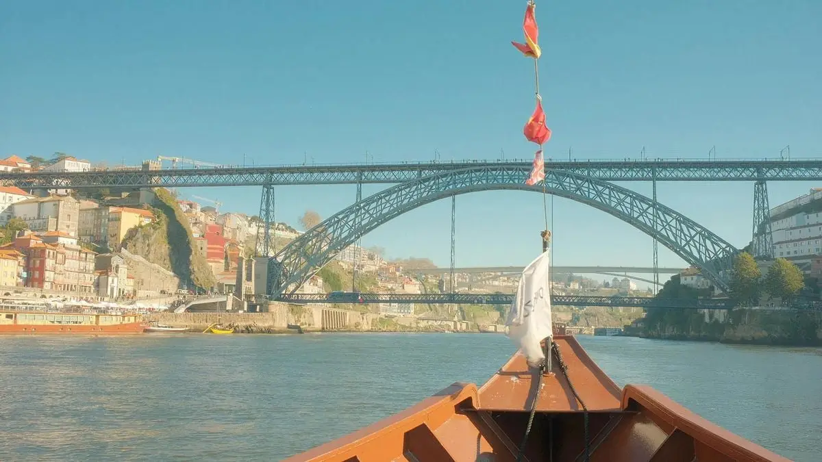 Scenic shot of the Dom Luís I Bridge viewed from a boat in Porto, Portugal, under a bright blue sky.