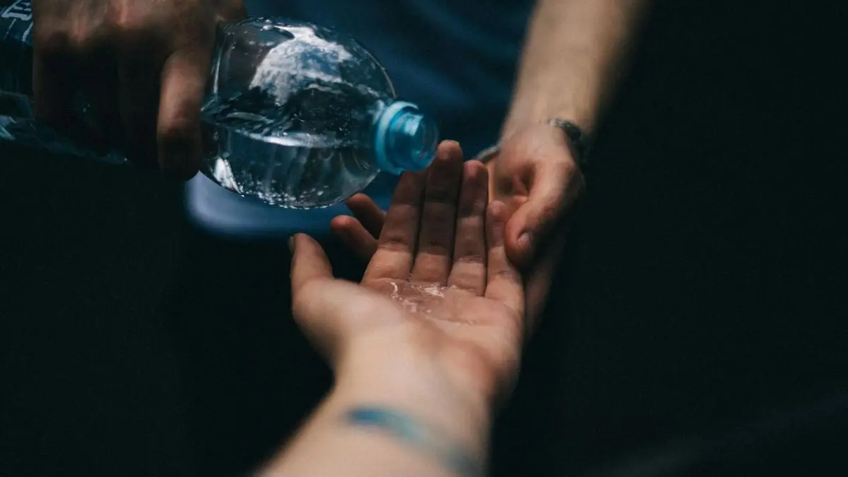Close-up shot of water being poured from a plastic bottle into open hands, emphasizing cleanliness and refreshment.