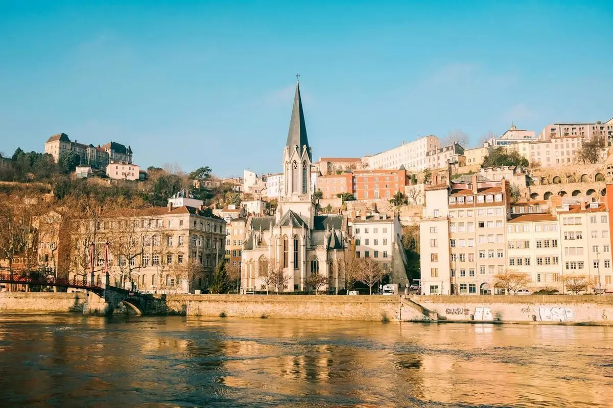 Scenic view of a historic church along the river with colorful buildings and clear sky.