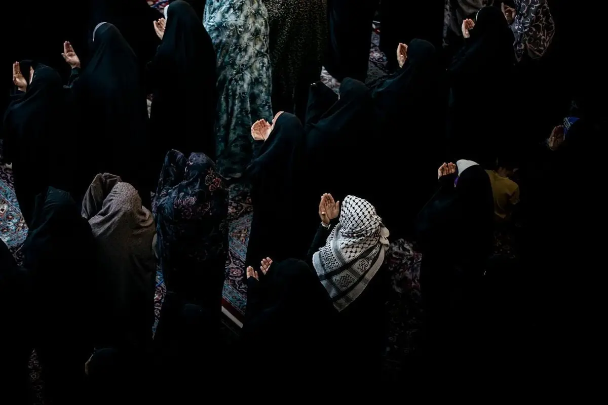 Muslim women in black attire praying during a religious gathering in Karbala, Iraq.