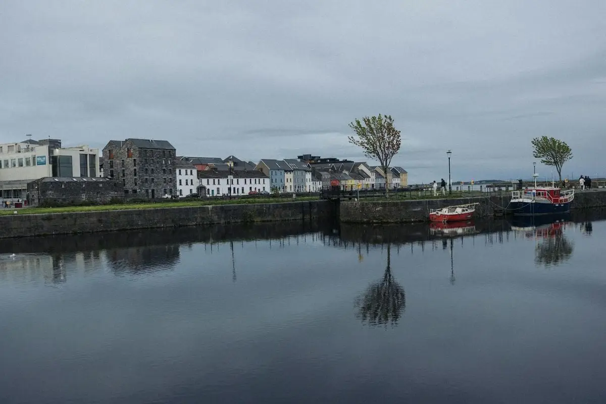 Serene harbor scene with colorful boats and historic buildings reflected in calm water.