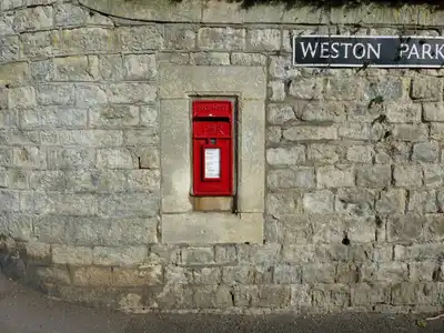 A classic red postbox embedded in a stone wall at Weston Park, Bath, UK.