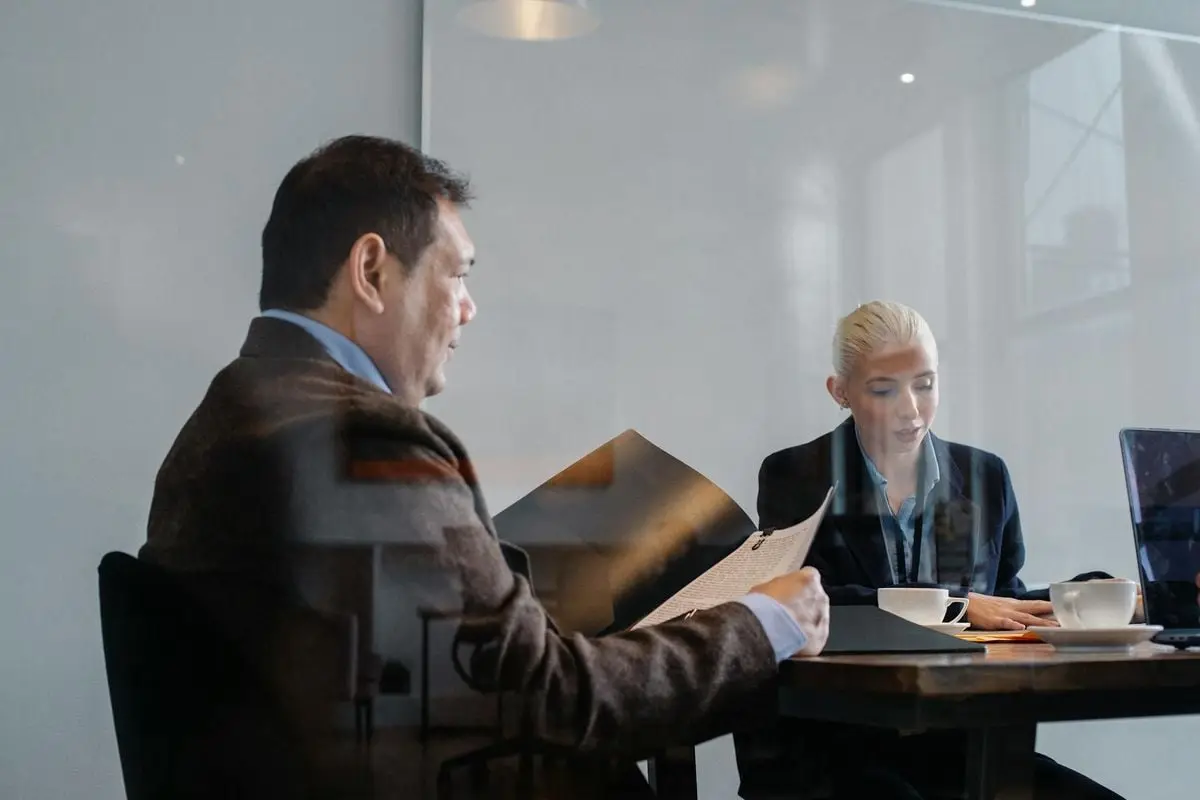 Diverse colleagues in formal clothes sitting at table and discussing details of business project in office