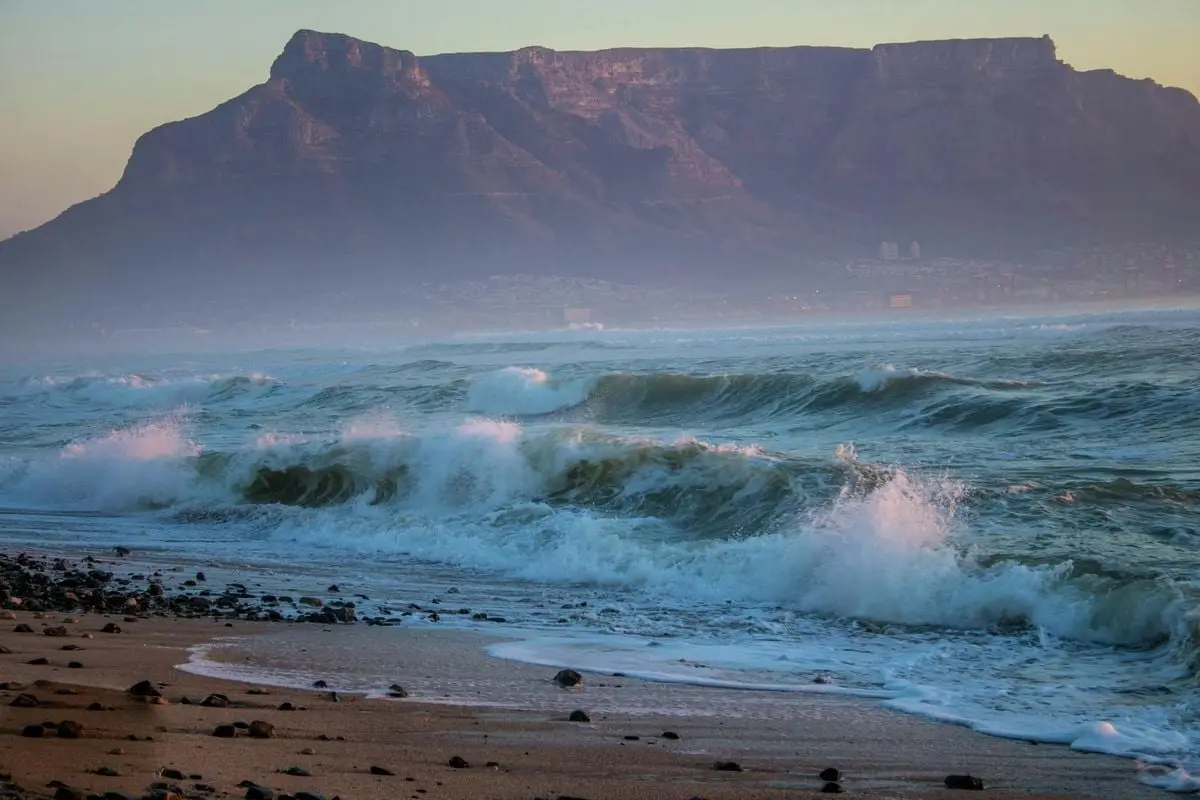 Stunning view of waves crashing on the shore with Table Mountain in the background at Cape Town, South Africa.