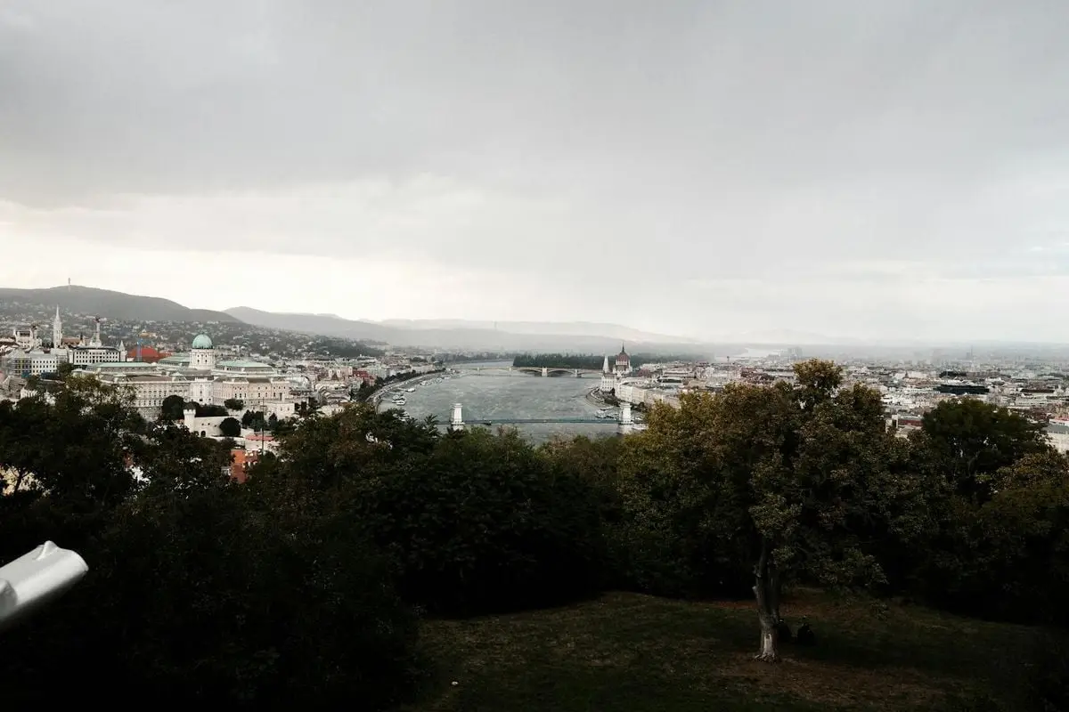 Panoramic view of Budapest cityscape with the Danube River and iconic buildings on a cloudy day.