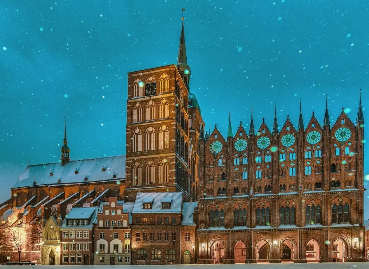 Captivating winter evening view of Stralsund Town Hall, Germany. Snowfall enhances the historic landmark's charm.