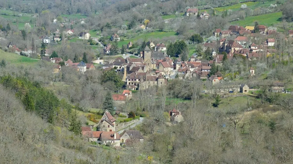 Aerial view of a picturesque European village surrounded by lush greenery and hilly terrain.