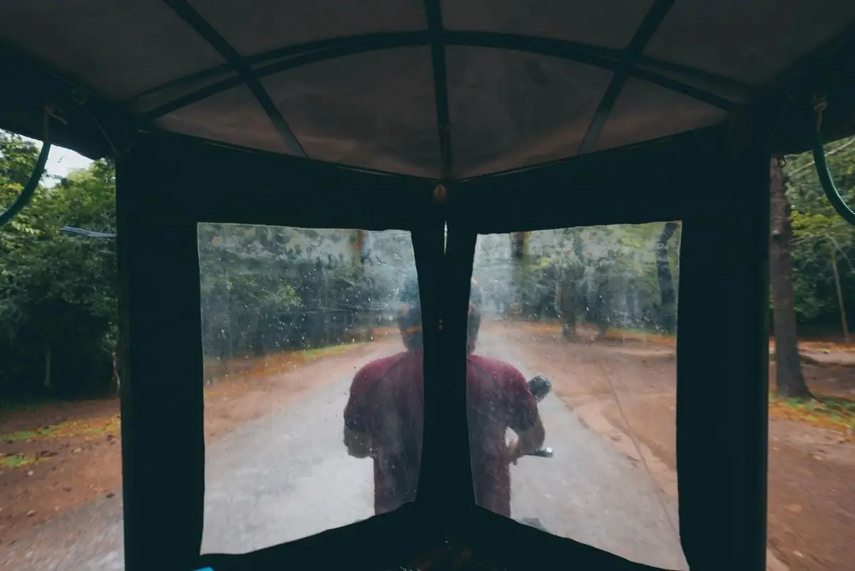 View from inside a tuk tuk driving through rainy Siem Reap, Cambodia, showcasing rustic countryside.