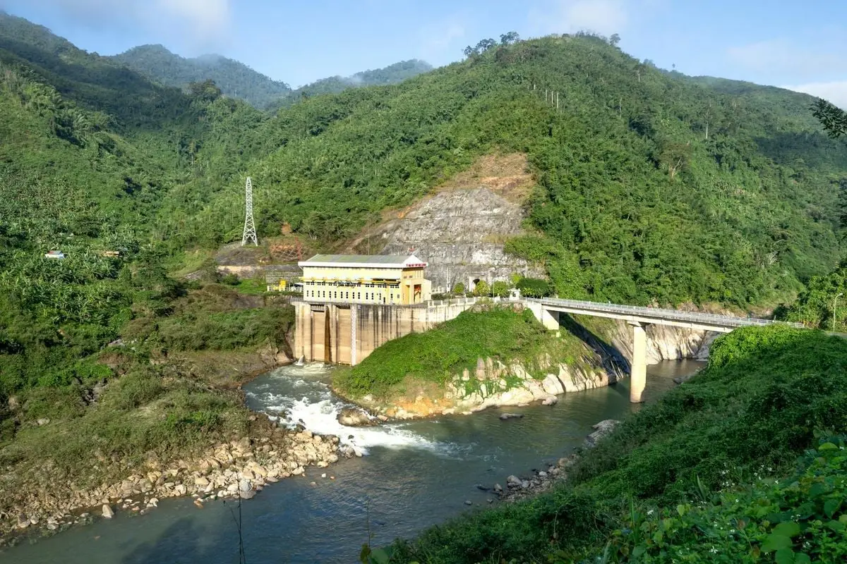 Scenic view of a hydroelectric power station amidst lush green mountains and a flowing river.