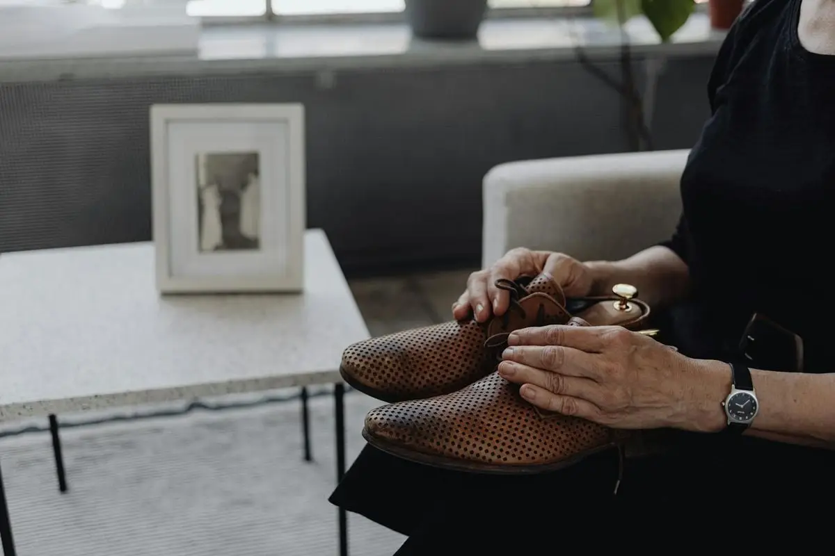 A person sits holding brown leather shoes, reflecting on memories.