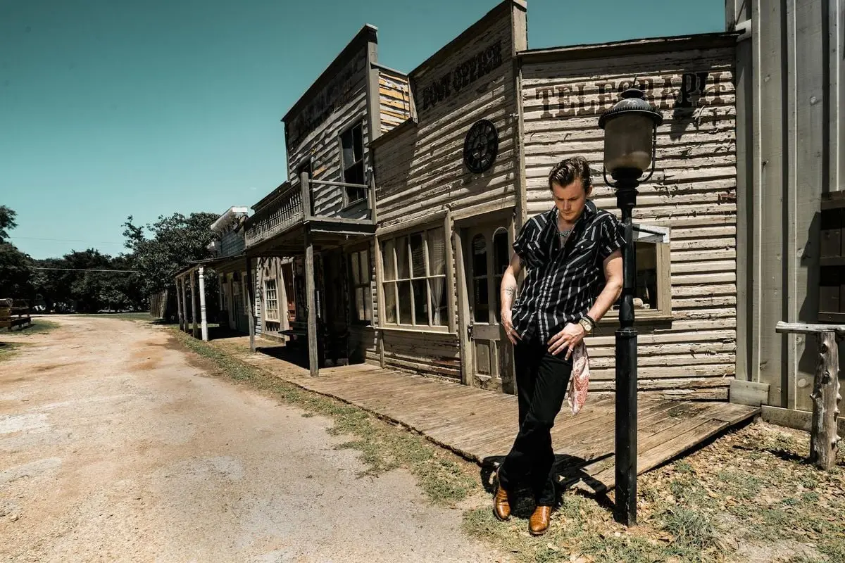 Man in western attire standing on a rustic street in Wimberley, Texas.