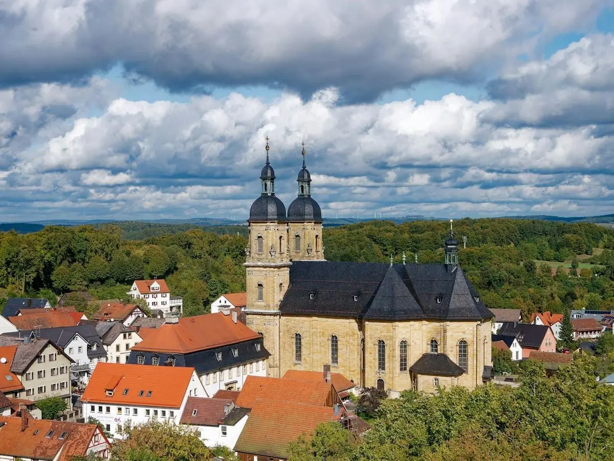 Aerial view of the Gößweinstein Basilica and quaint town in Bavaria under dramatic clouds.