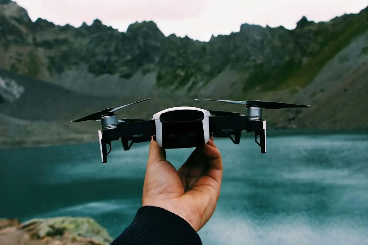 Unrecognizable traveler demonstrating modern drone against calm lake and mountain ridge in countryside