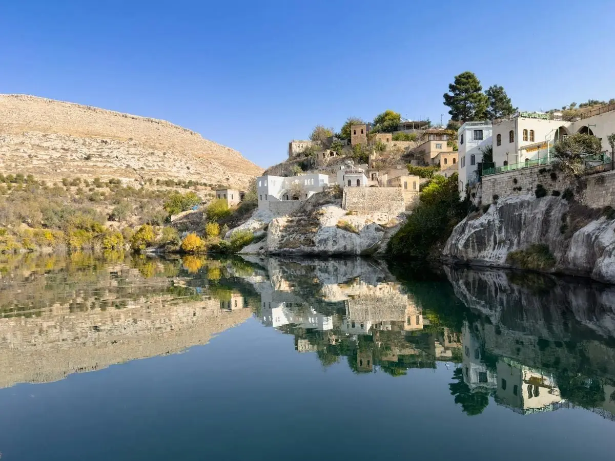 Picturesque Halfeti river scene with historic buildings reflected in calm waters.