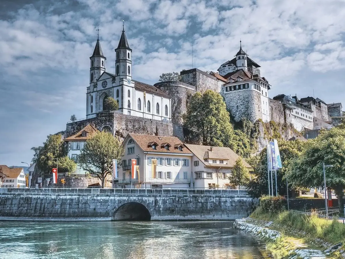 Stunning view of Aarburg Castle in Switzerland across Aare River with clear sky and trees.