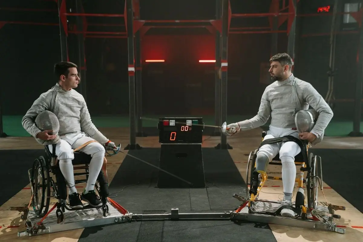 Adaptive fencing match between two athletes in wheelchairs, showcasing determination and skill indoors.