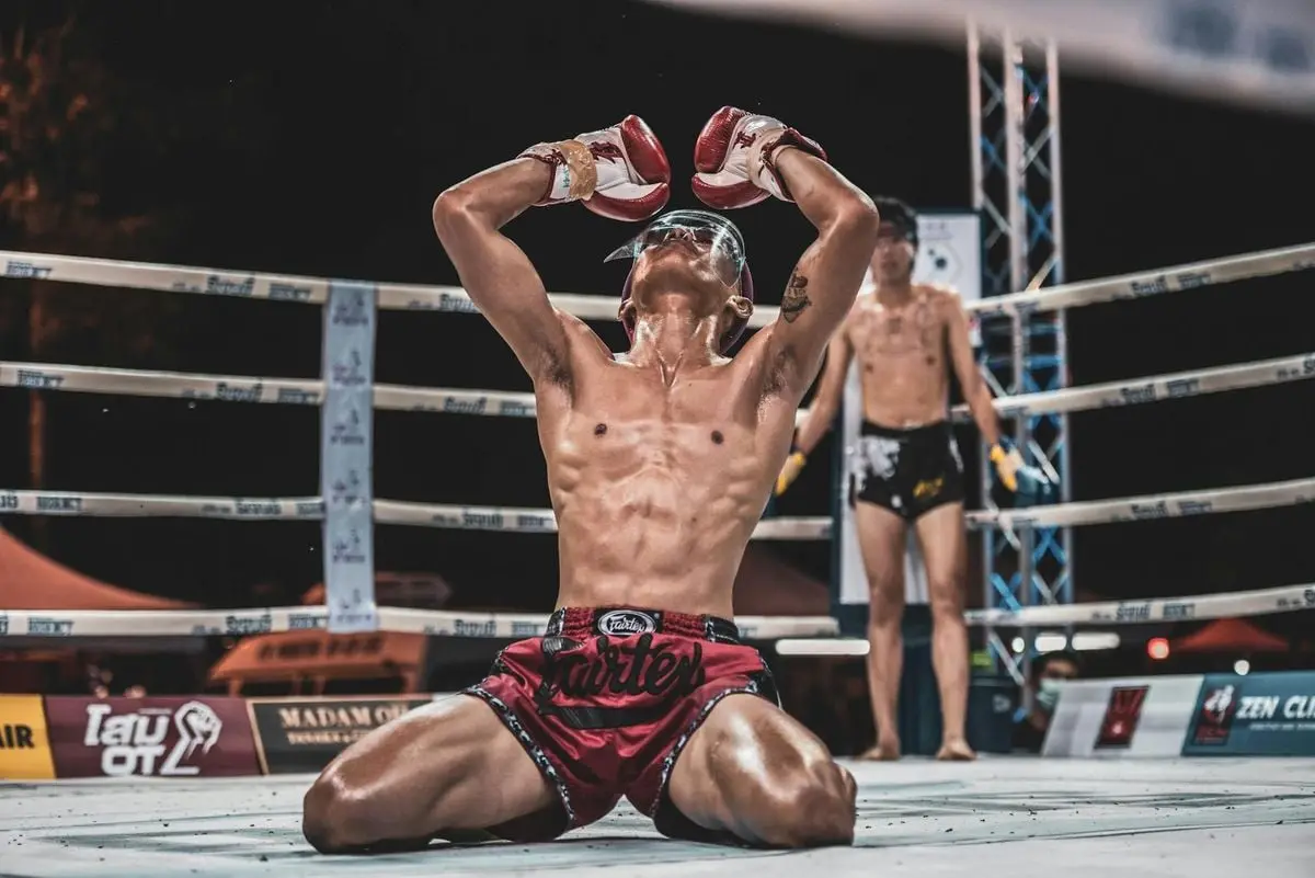 A triumphant boxer kneels in the ring, expressing victory with raised gloves.