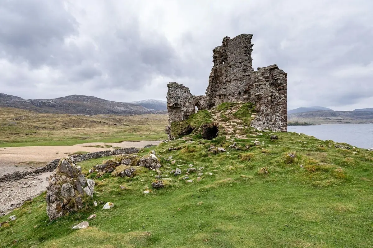 Explore the historic Ardvreck Castle ruins set amidst the scenic Highlands in Scotland, under a moody sky.