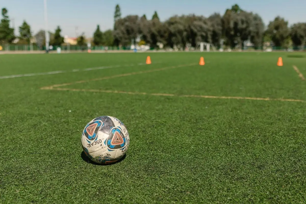 A soccer ball on a green field with training cones under a clear sky.