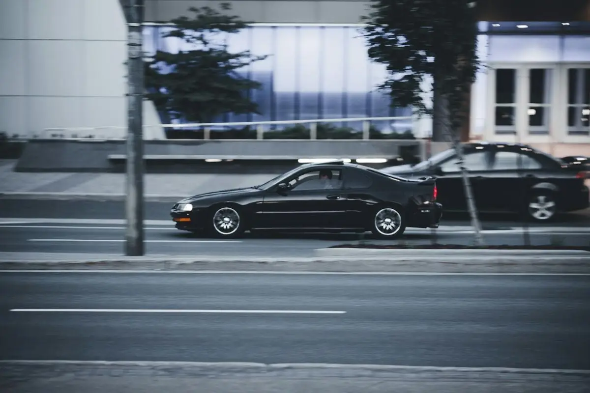 A black car moves swiftly along a city road with blurred background indicating speed and motion.